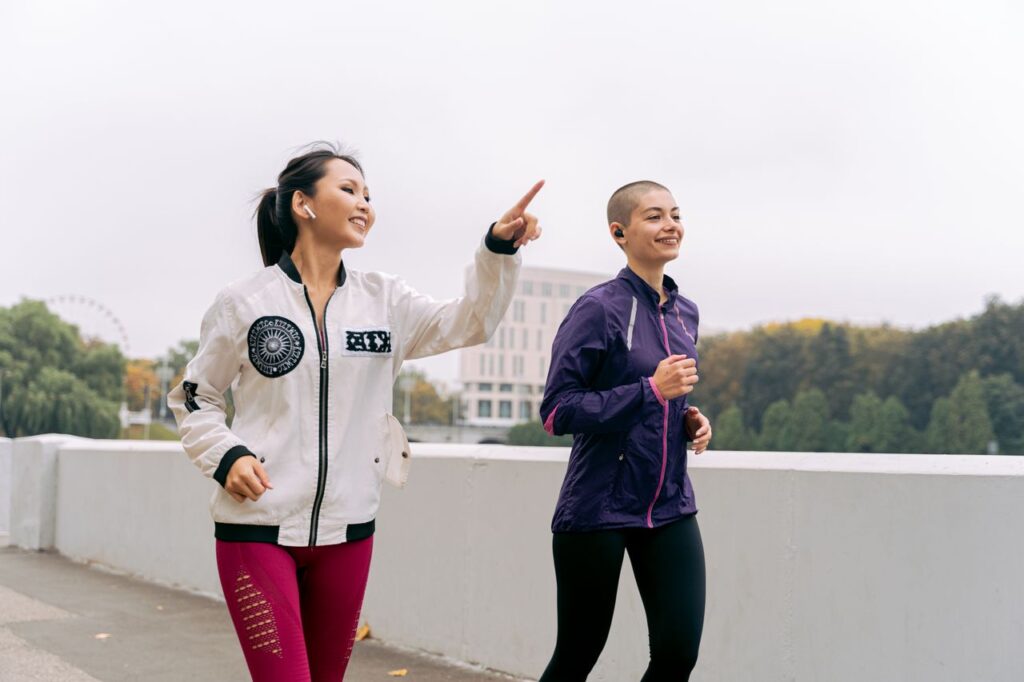 Two women jogging outdoors in fall, promoting fitness and healthy lifestyle.